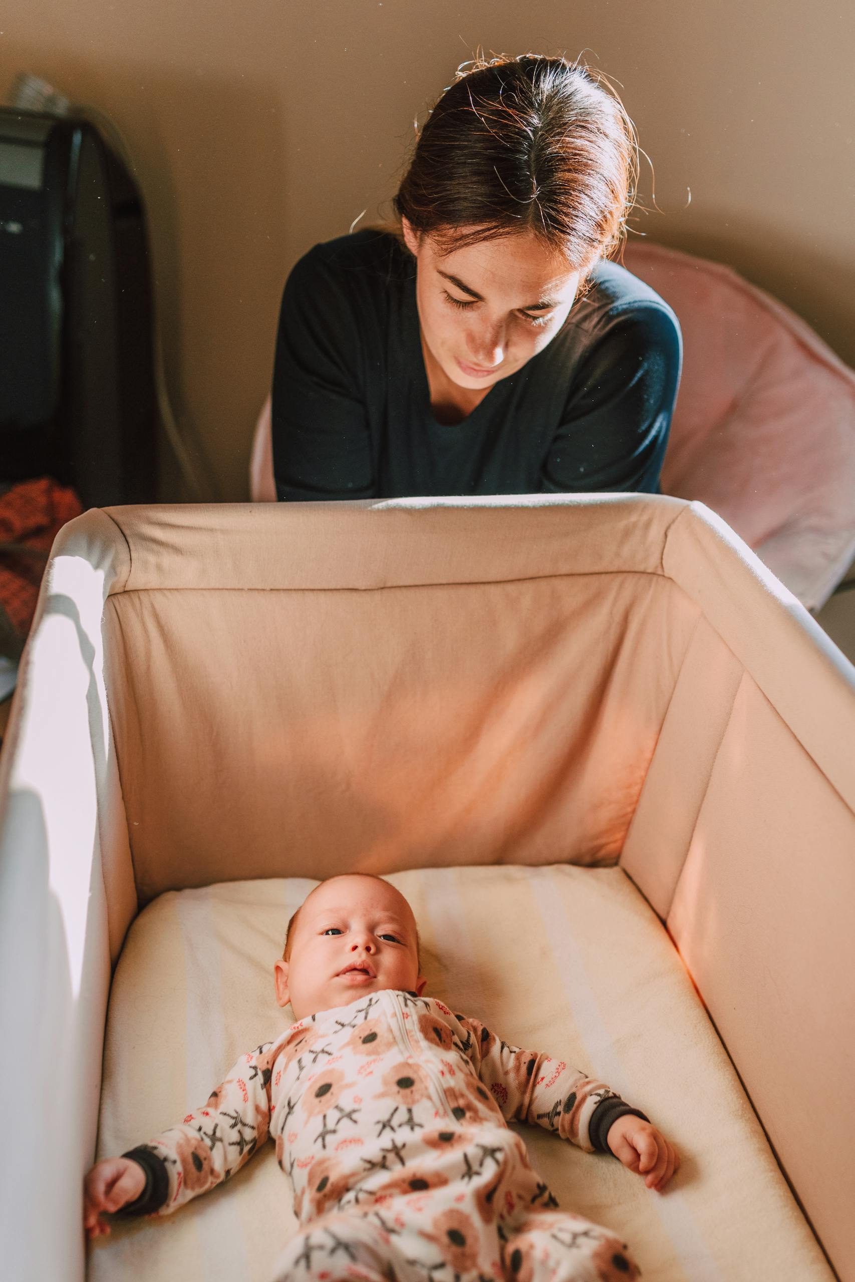 A mother lovingly watches her baby in a crib, capturing a tender parent-child moment indoors.